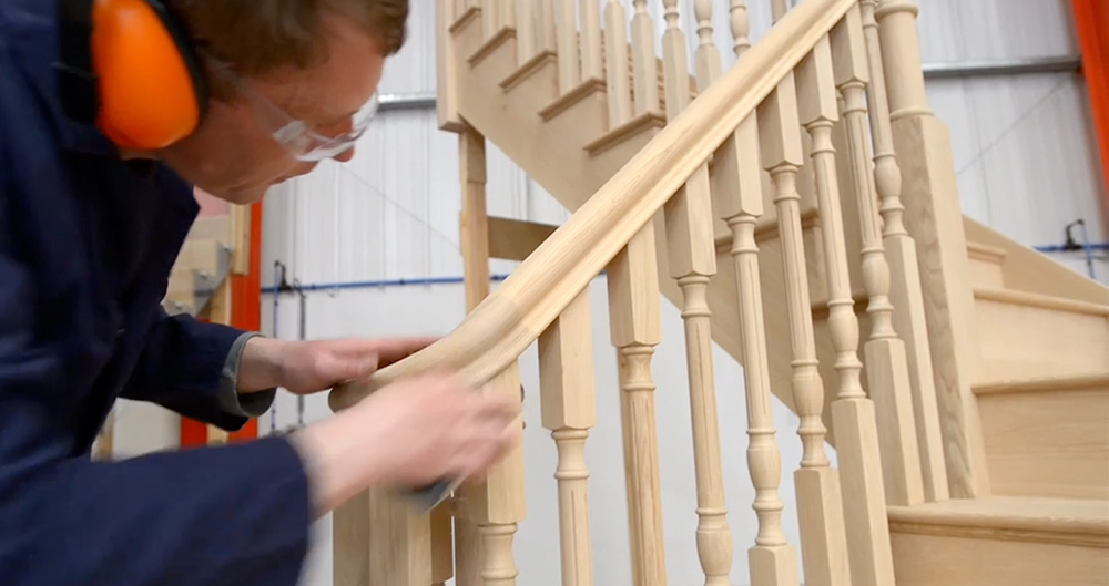Craftsman fine sanding a handrail volute in the Stairplan workshop